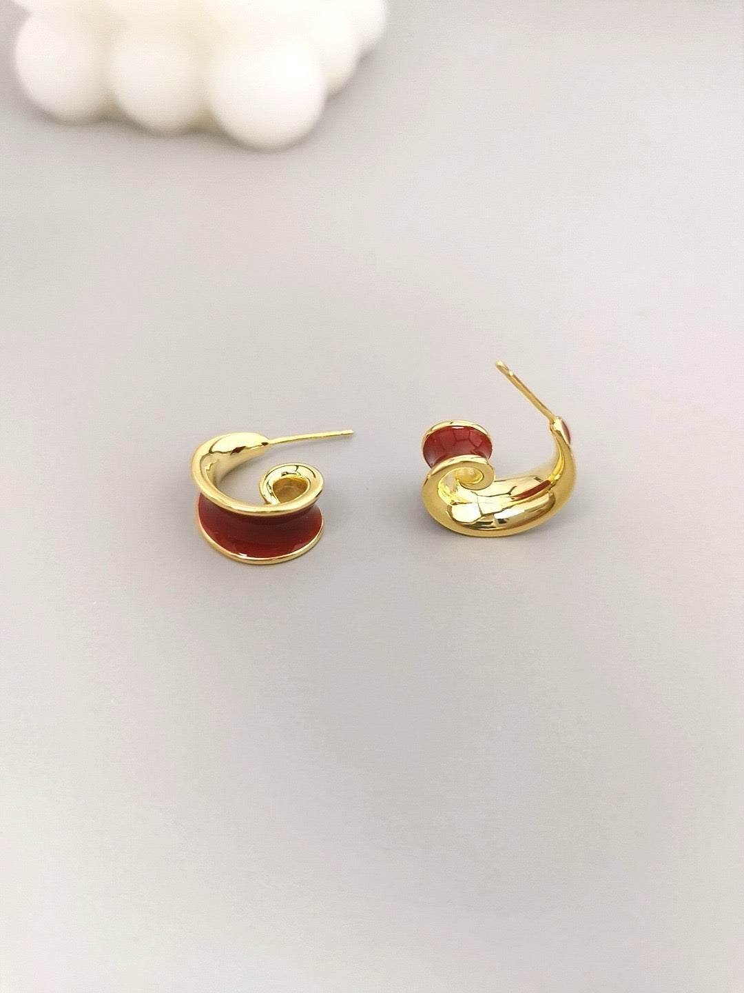 Gold earrings with red enamel on a light gray background