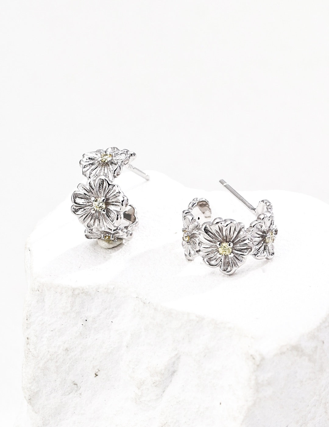 Pair of sterling silver floral earrings with zircon on a textured white surface