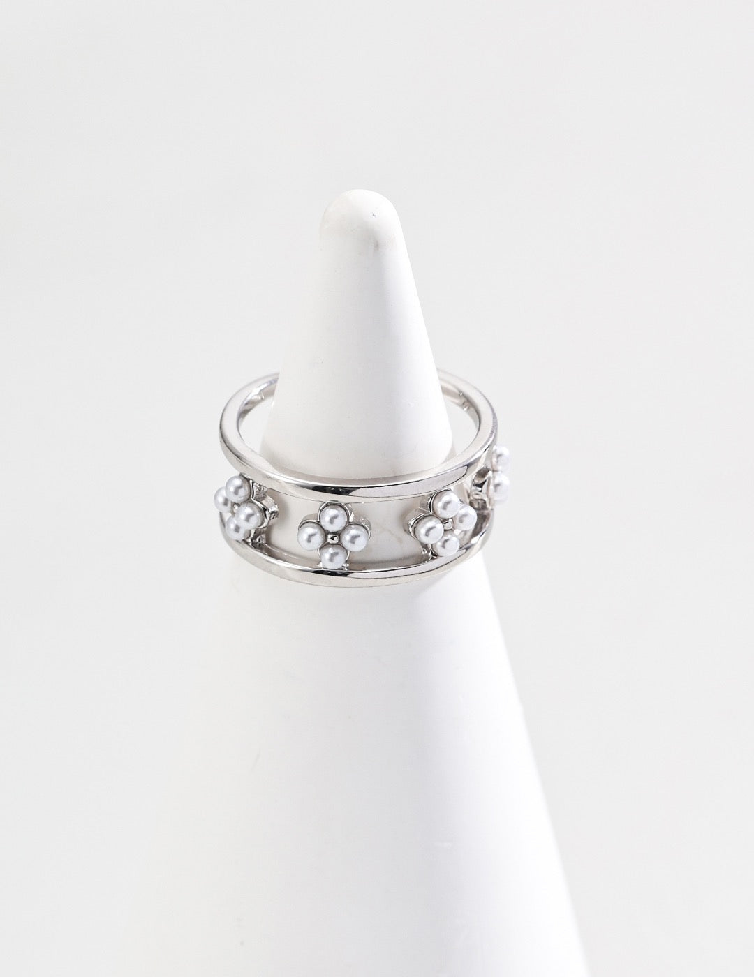 A close-up of the sterling silver open ring with a floral design adorned with small freshwater pearls, displayed on a white cone-shaped jewelry holder against a clean white background.