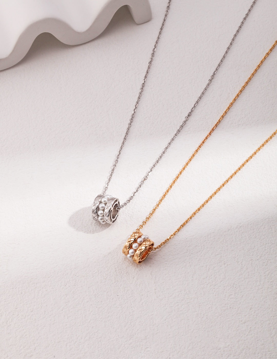 Two necklaces, one silver and one gold, on a light gray surface.