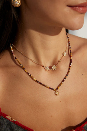 A model is wearing the Gold Floral Charm Necklace, layering with the gemstones necklace. 