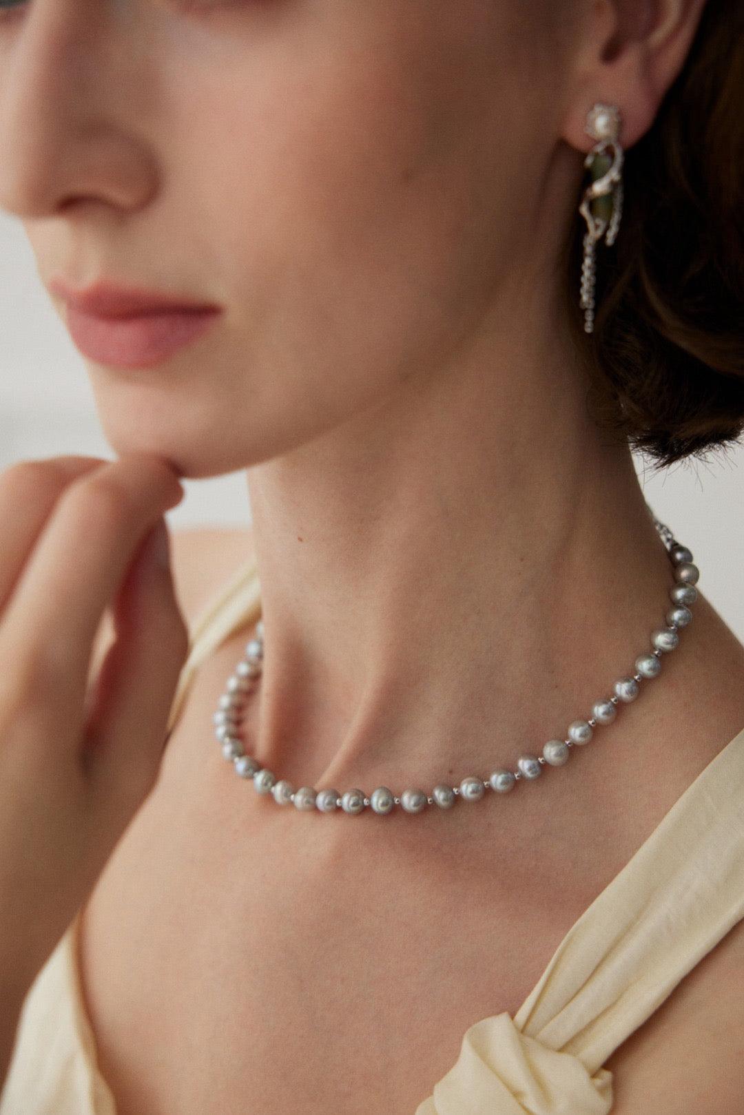 A woman wearing a grey pearl necklace and matching earrings, with the necklace being the main focus.