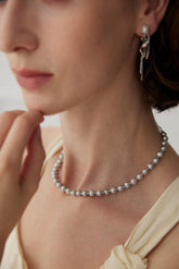 A woman wearing a grey pearl necklace and matching earrings, with the necklace being the main focus.