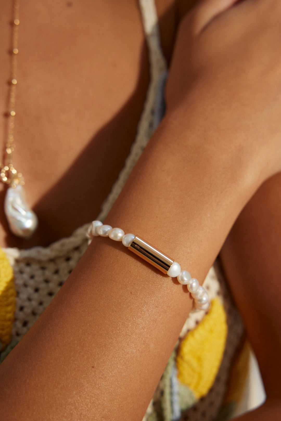 The lady is wearing the Allison Bracelet features a refined strand of lustrous 6mm freshwater pearls elegantly interrupted by a sleek cylindrical 18K gold vermeil accent piece