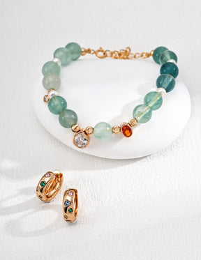 Bracelet with green aquamarines, zircon charm and gold accents on a white surface