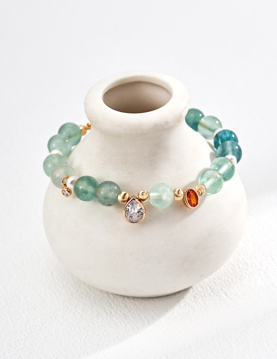 Aquamarine Gemstone bracelet with gold accents on a small white vase against a white background