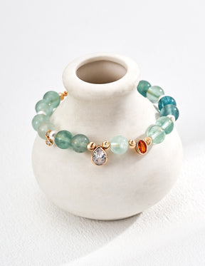 Aquamarine Gemstone bracelet with gold accents on a small white vase against a white background