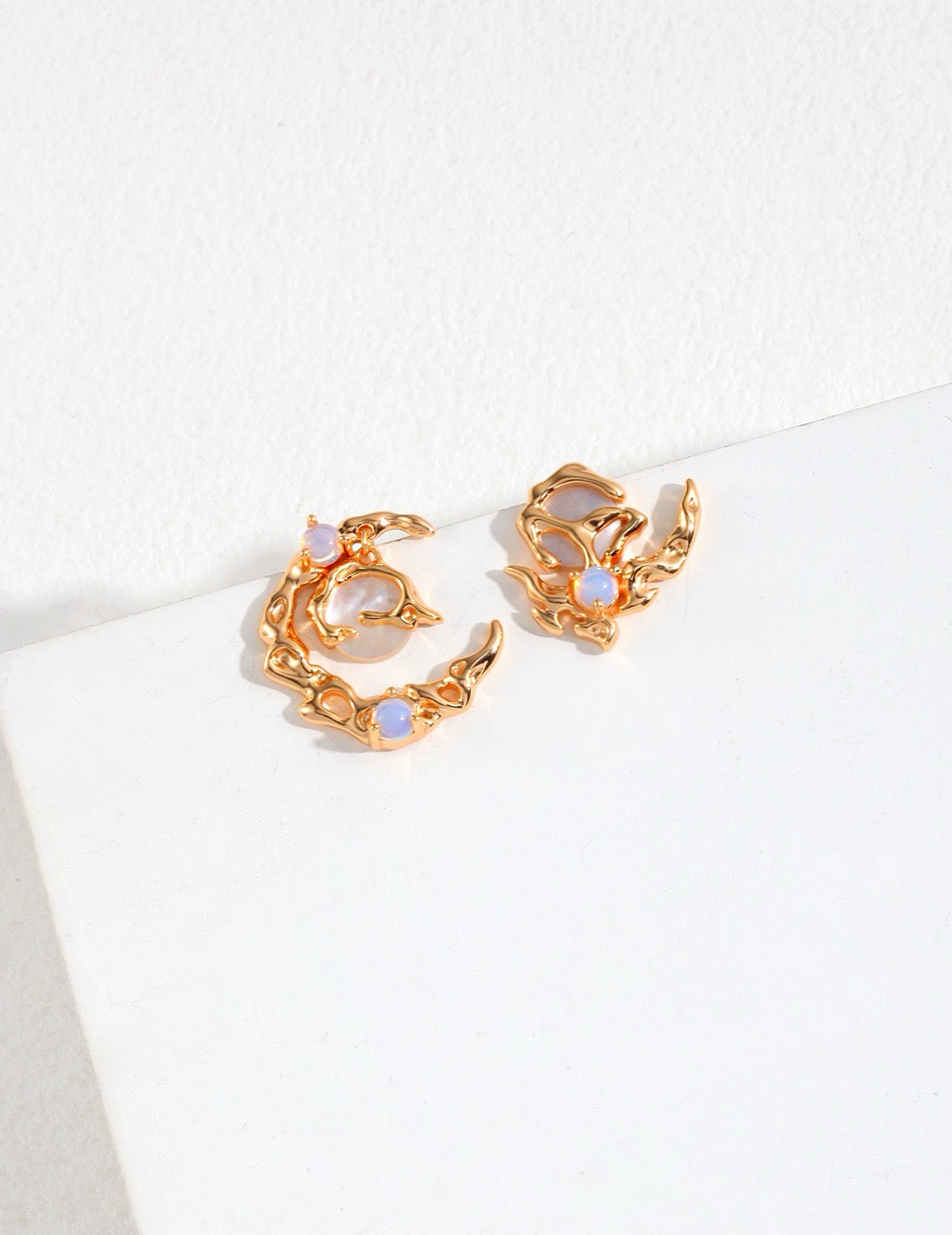 Gold asymmetrical hoop earrings with opal stones on a white background