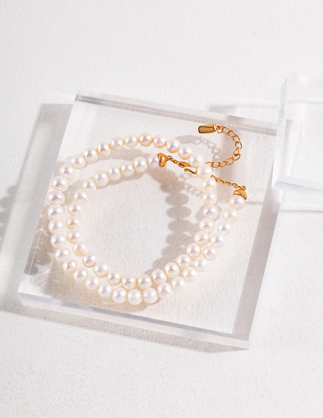 7mm Freshwater Pearl strand necklace with gold clasp on a clear display box against a white background