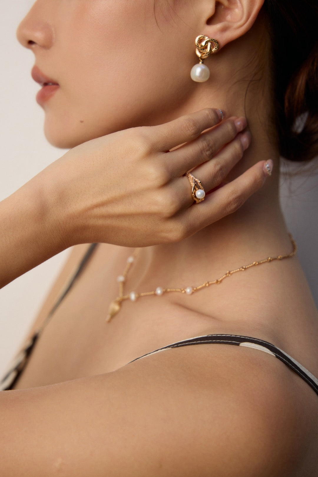 Close-up of a person wearing gold jewelry with pearl accents on a neutral background