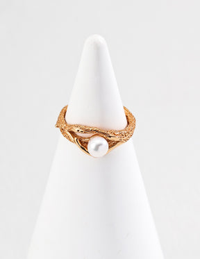 Gold pearl ring with a pearl on a white stand against a light gray background