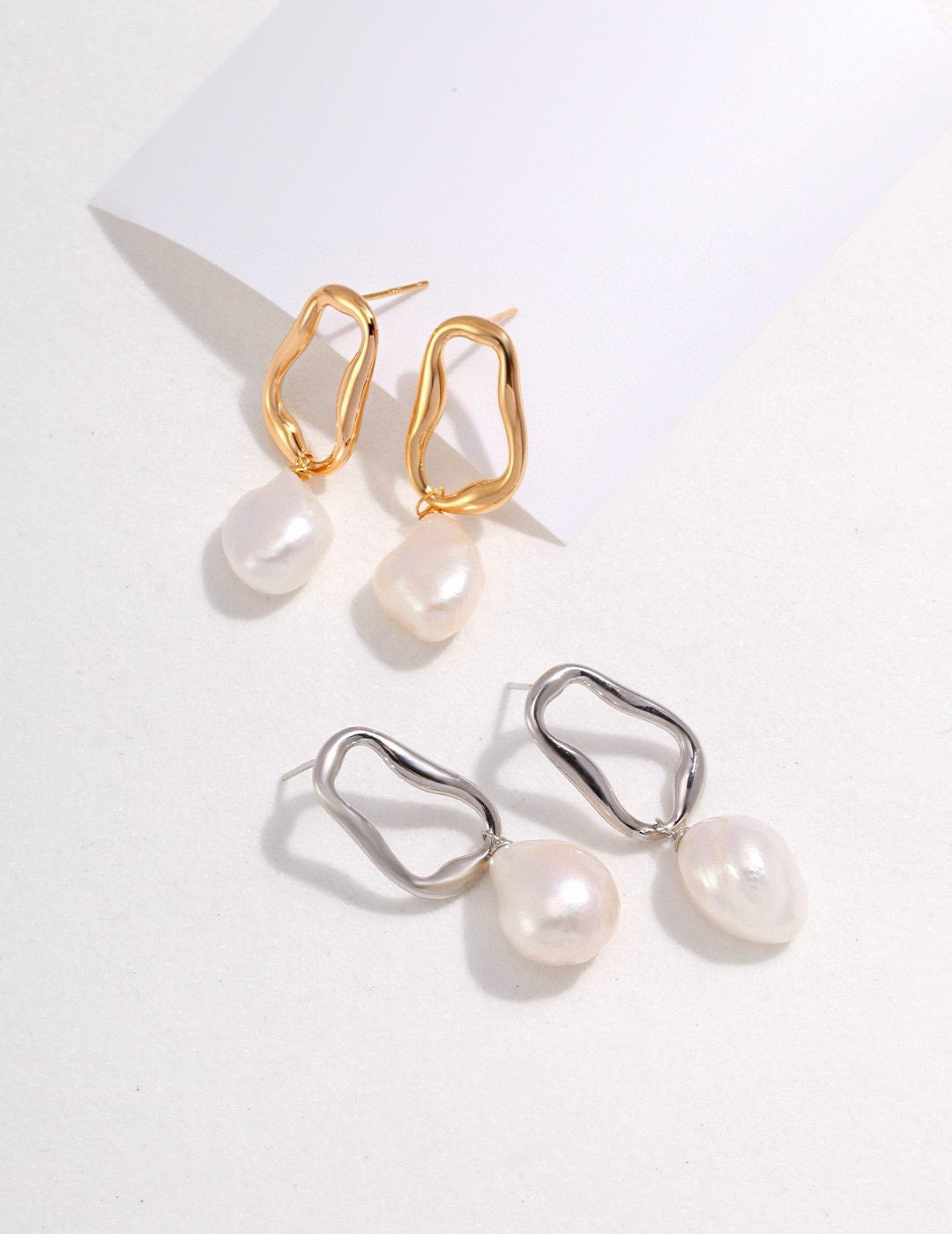 Aurora Baroque Pearl Drop Earrings feature naturally irregular 12-14mm baroque pearls suspended from fluid, sculptural hoops in luxurious 18K gold vermeil or sterling silver displayed on the white background. 