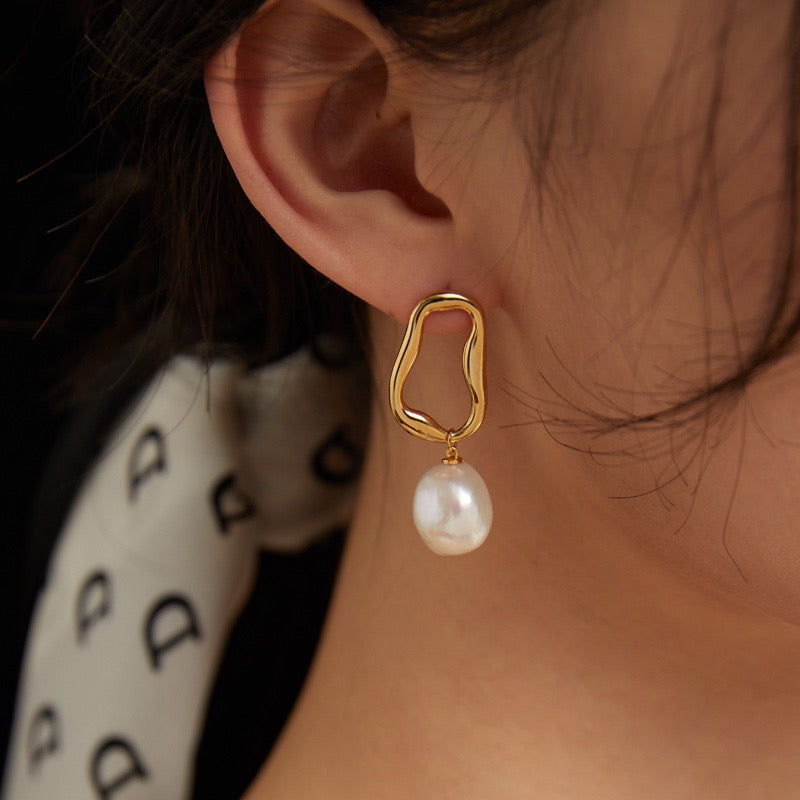 The Aurora Baroque Pearl Drop Earrings feature naturally irregular 12-14mm baroque pearls suspended from fluid, sculptural hoops in luxurious 18K gold vermeil wear by a woman.