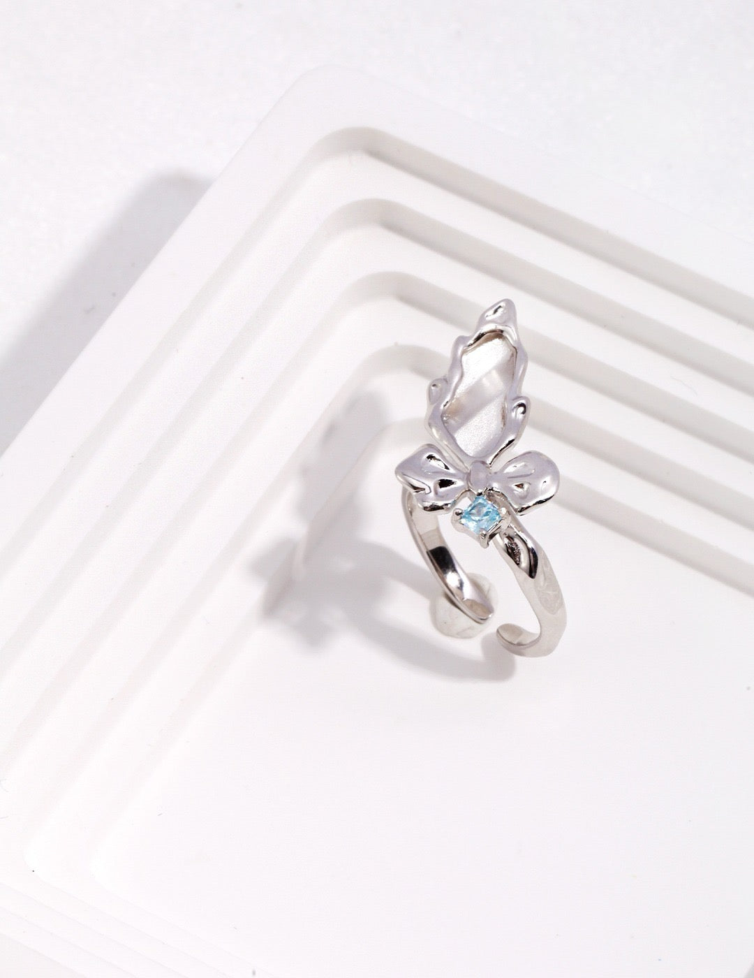 Silver ring with a butterfly design and blue gemstone on a white background