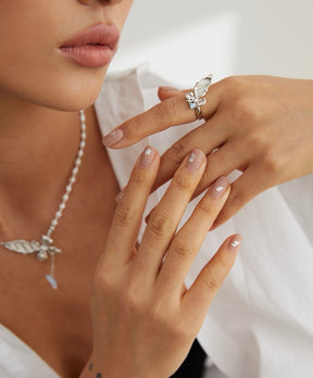 Close-up of a woman's hands with a ring and necklace, wearing a white top.