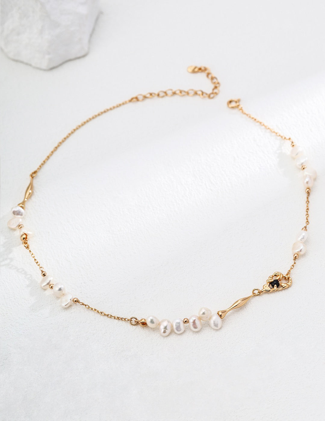 A delicate Aurora Freshwater Pearl Necklace featuring irregular freshwater pearls, an 18K Gold chain, and a black agate accent, styled on a white background.