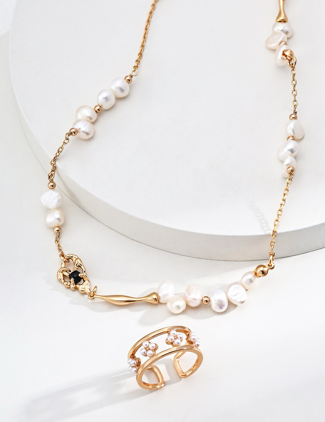 A Aurora Freshwater Pearl Necklace adorned with freshwater pearls and a black agate pendant, displayed with a matching open-band ring featuring delicate pearl flowers, set against a white backdrop.