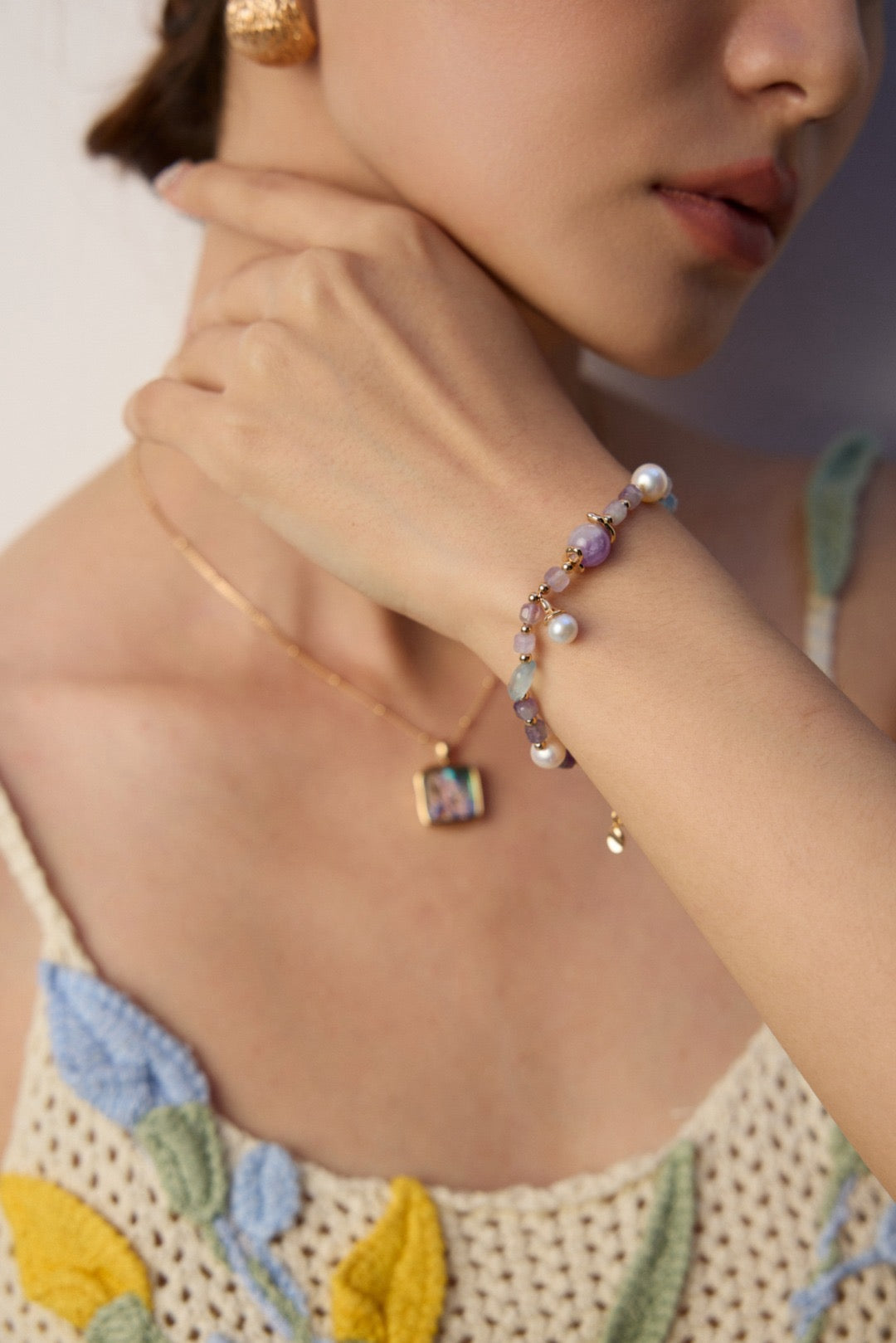 Close-up of a person wearing a gold necklace and pearl bracelet on a blurred background