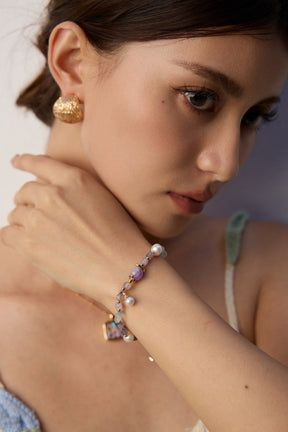 Woman wearing gold earrings and a colorful bracelet on a plain background