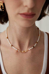 A close-up image of a woman wearing a Tiger Eye and Pearl necklace with gold accents around her neck.