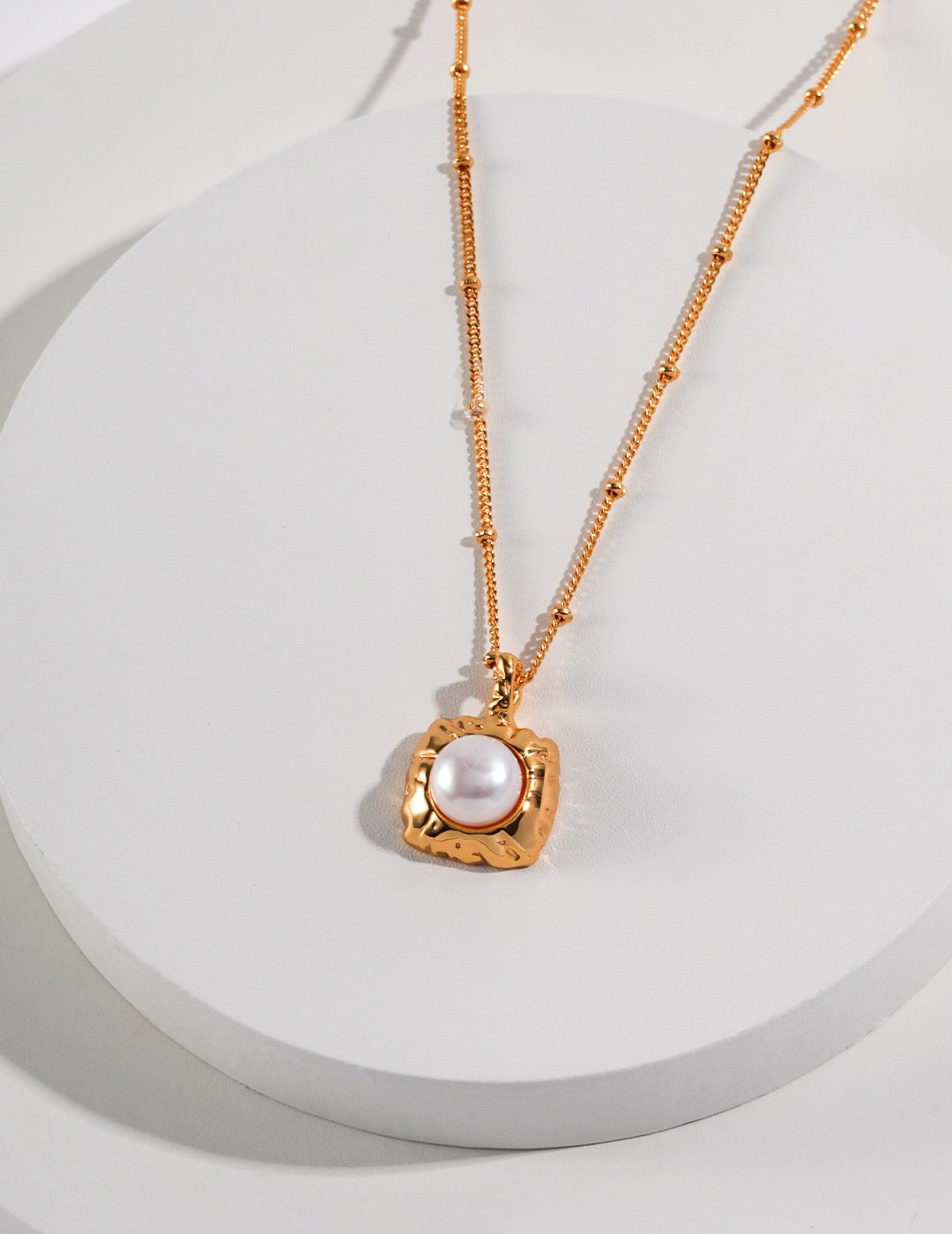 Gold necklace with a pearl pendant on a white background