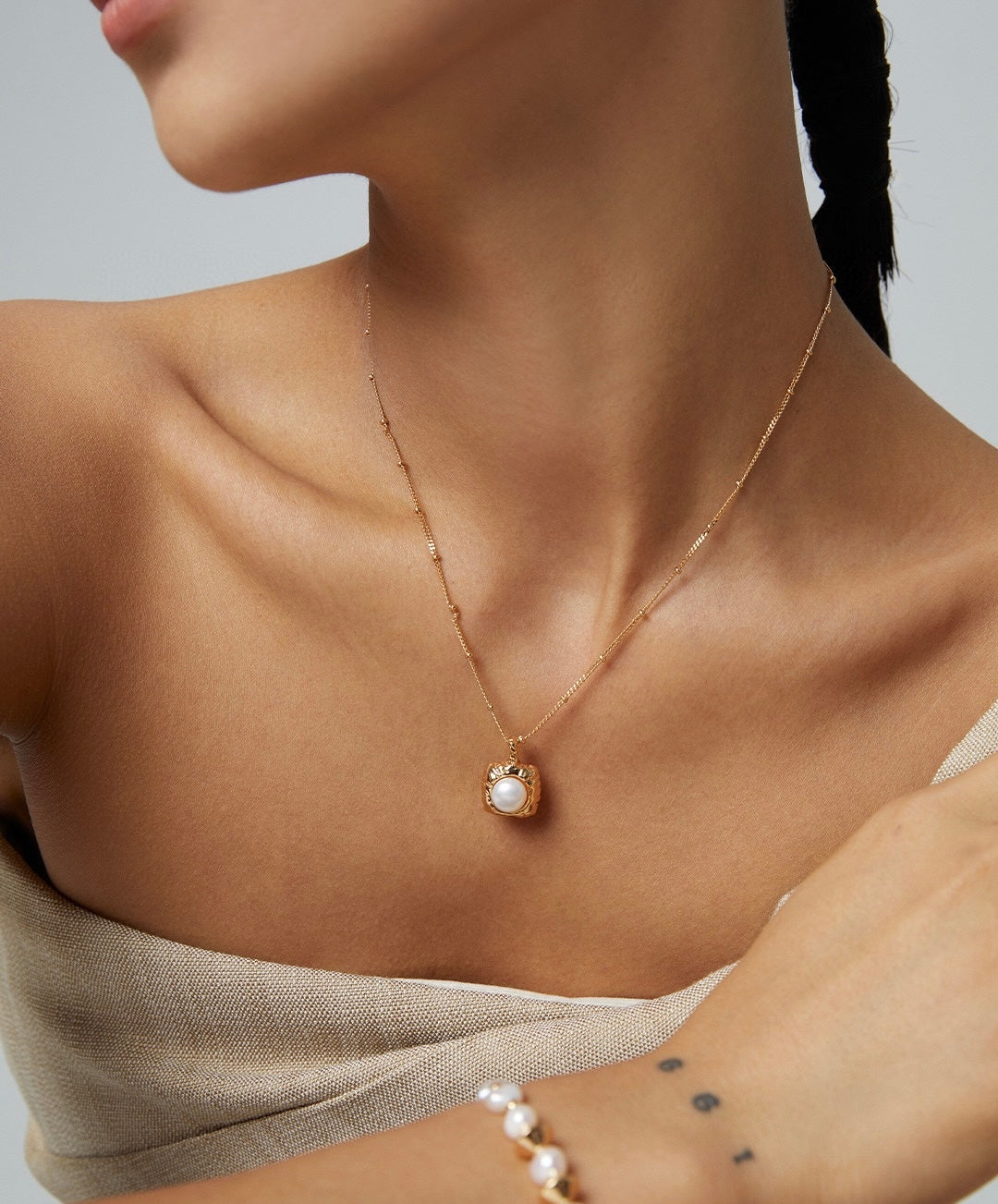 Necklace with a pearl pendant worn by a person on a neutral background