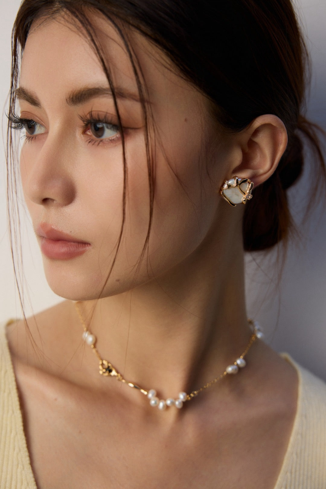 A person wearing baroque pearl earrings with gold details and a matching necklace.