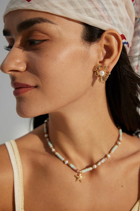 A person wearing a floral pearl earrings with gold detailing.