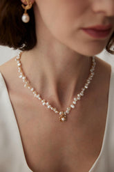 A person wearing a white garment showcasing a gold necklace with pearl beads and a camellia-shaped pendant.