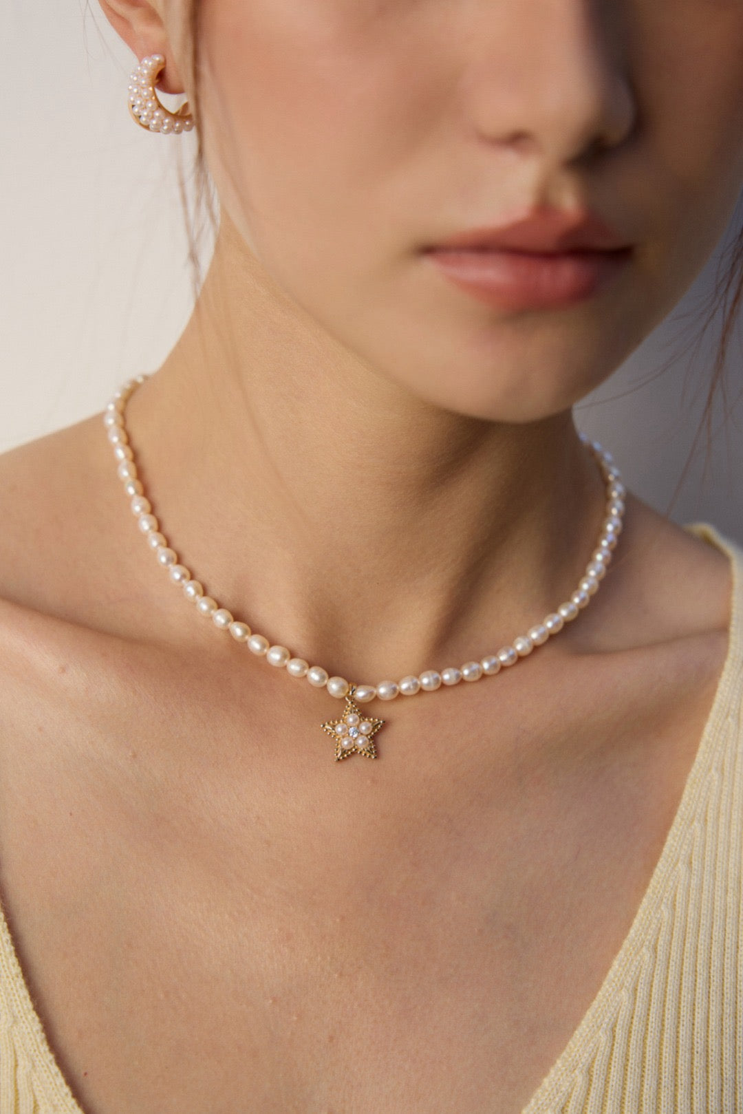 Pearl necklace with a star-shaped pendant worn by a person against a neutral background