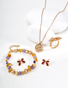 Gold bracelet with colorful gemstones and charms, necklace, and ring on a white background