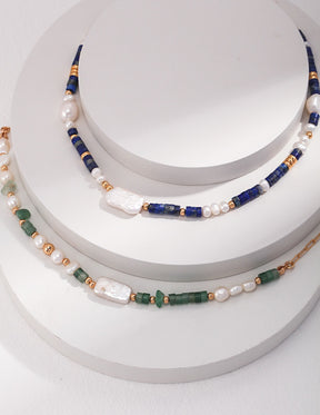 Three pearl necklaces with blue, green, and gold beads on a white surface