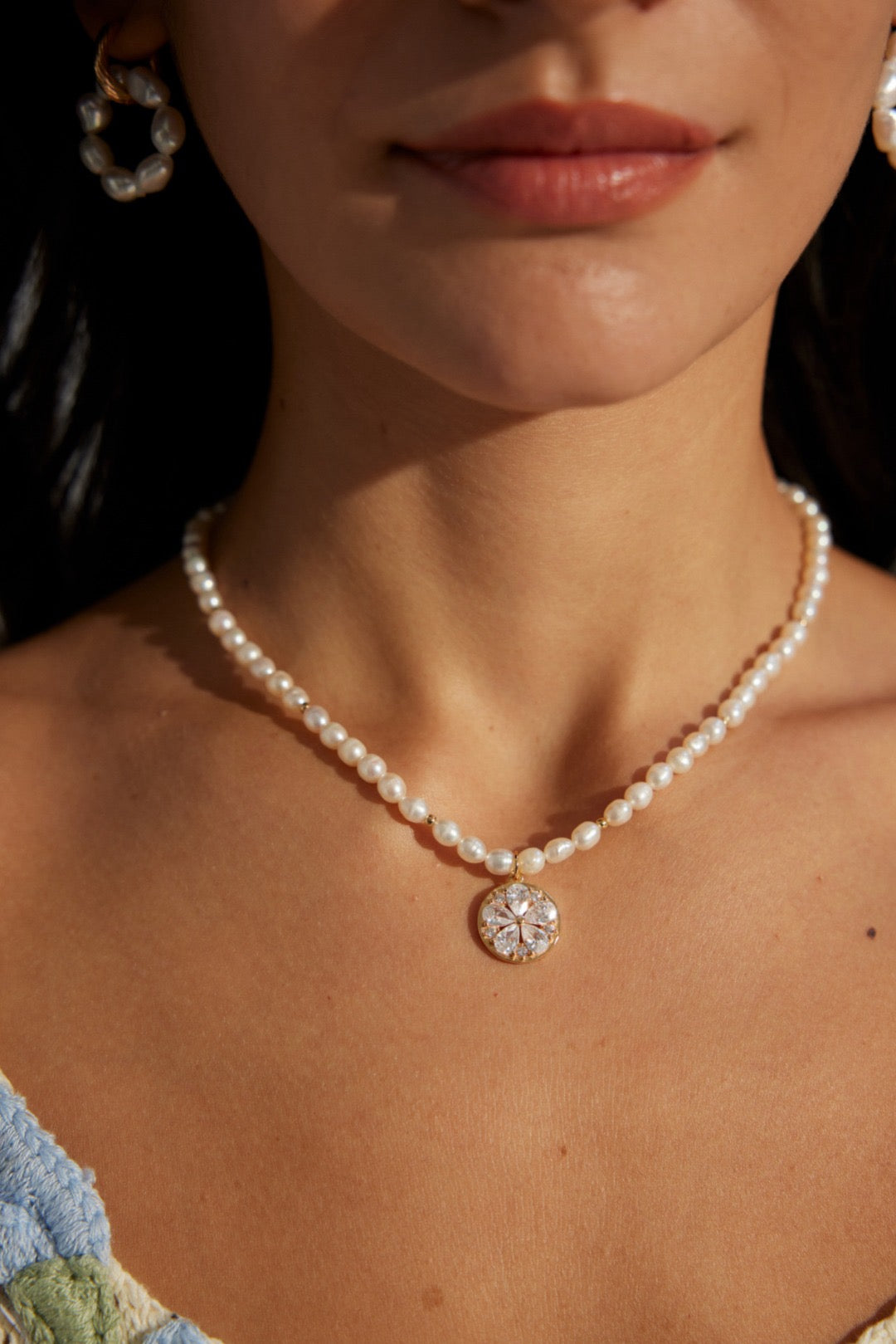 A person wearing a necklace with white pearls and a gold vermeil zircon flower pendant.