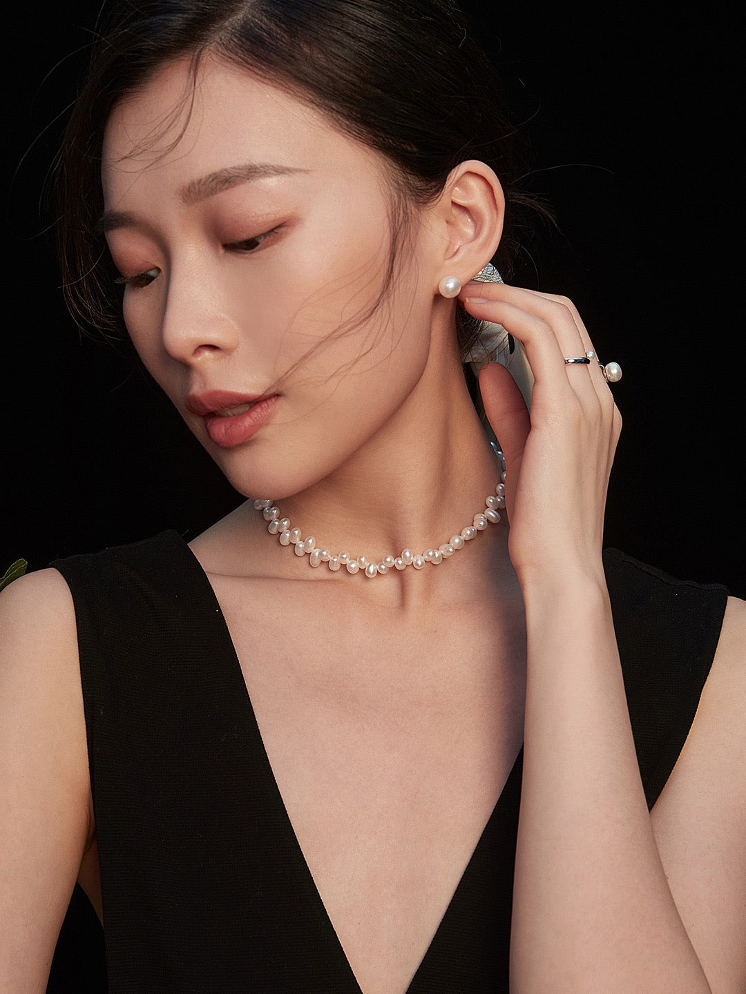 Woman wearing a pearl necklace and earrings against a black background