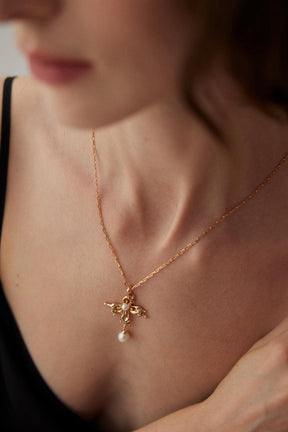 Close-up of the model wearing the Gold Charlotte Pearl Pendant Necklace, styled with the black deep v dress.