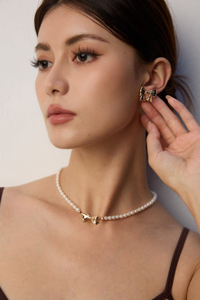 Woman wearing a pearl necklace and gold earrings against a neutral background
