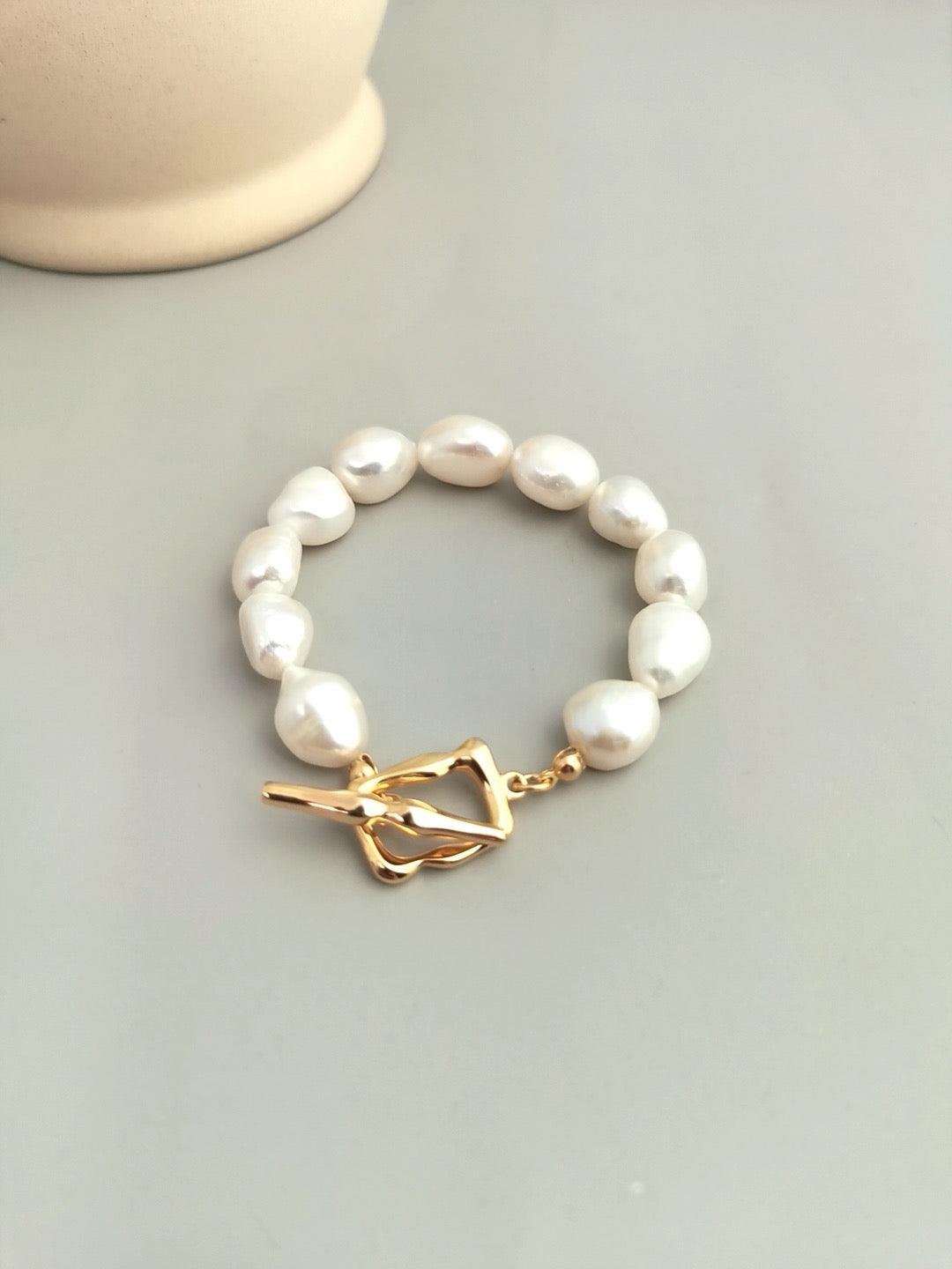 Crescent Baroque Bracelet featuring unique natural baroque pearls with elegant gold toggle closure displayed on the grey background.