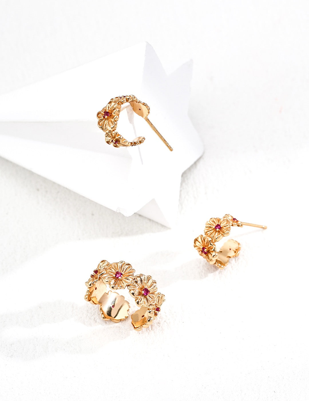 Gold floral earrings and daisy cuff ring with red gemstones on a white background