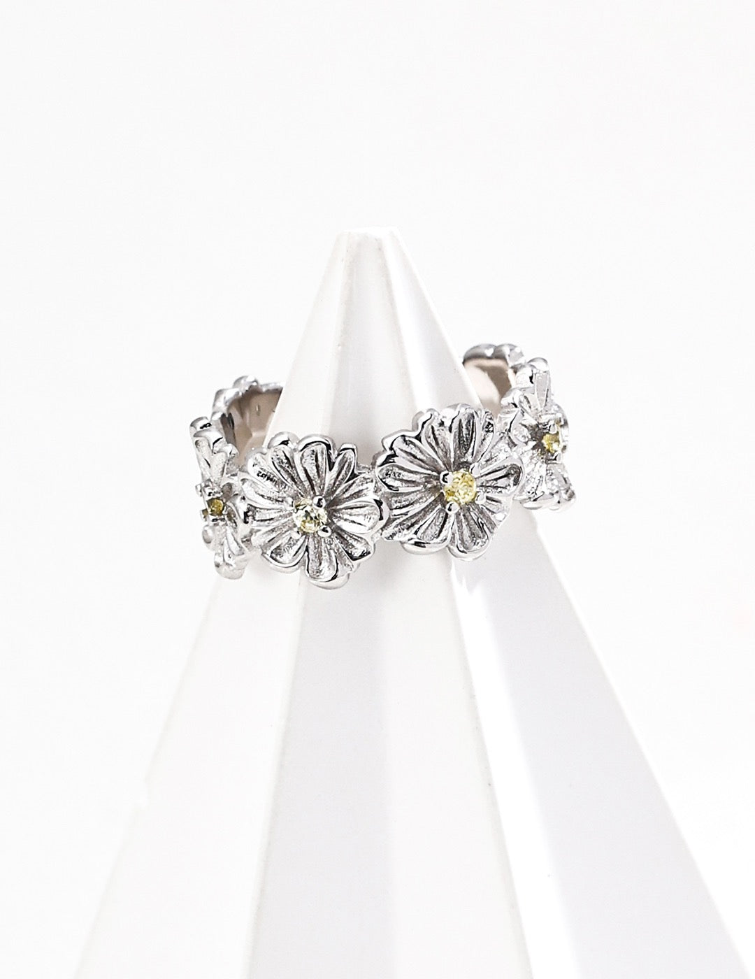 A silver floral cuff ring on a white stand