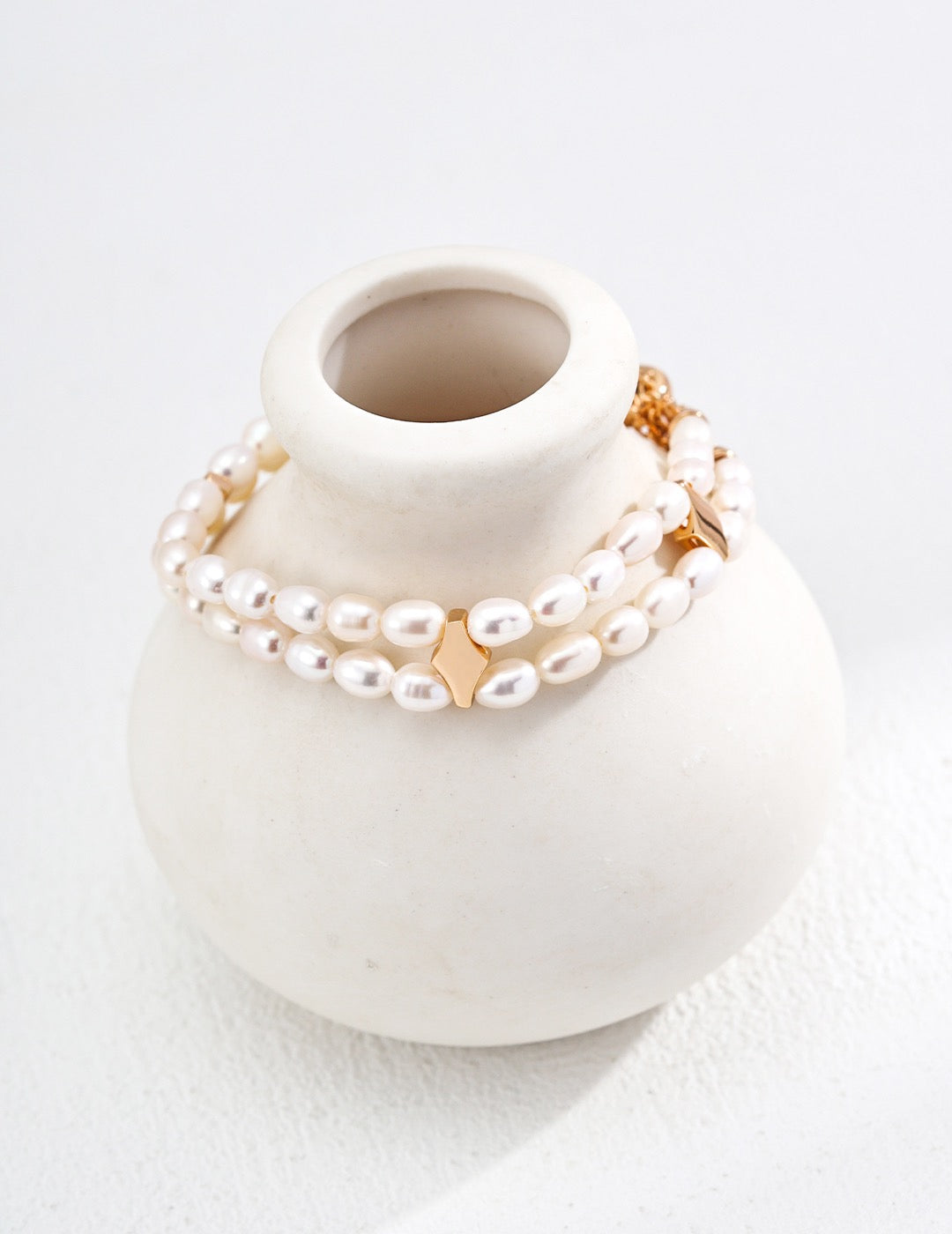 Pearl and gold bracelet on a white ceramic vase