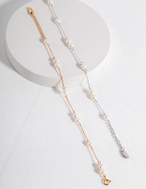 Gold and silver chain bracelets with freshwater pearls displayed on a white surface