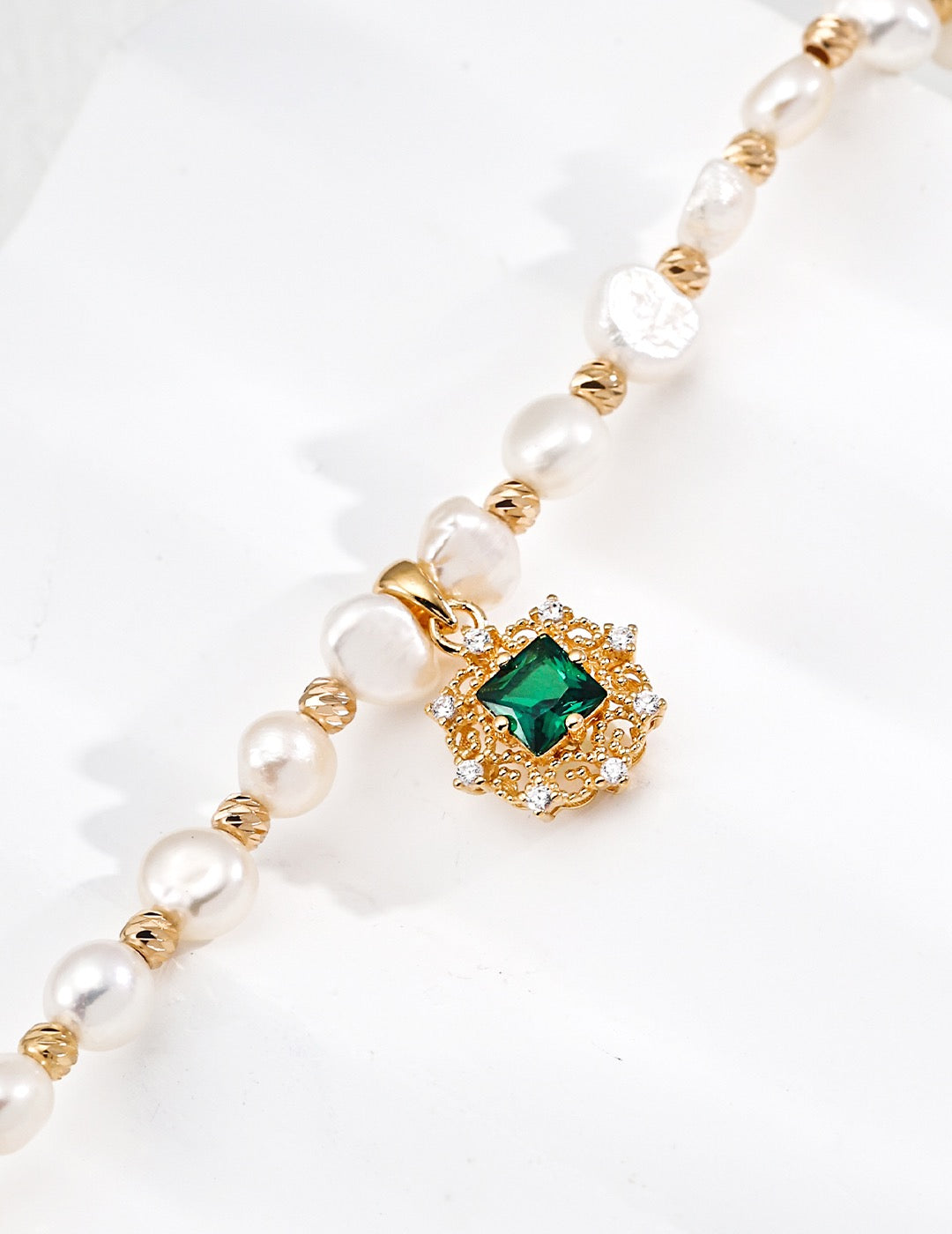 Pearl bracelet with a gold clasp and green gemstone on a white background