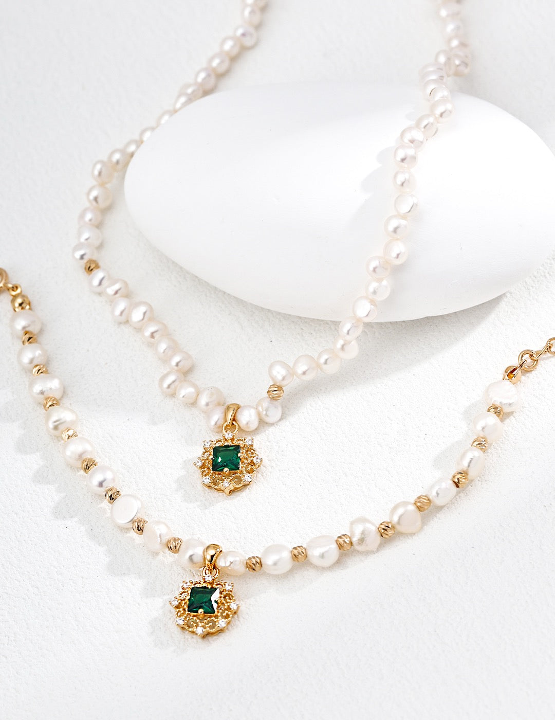Pearl necklace with gold accents and green gemstones on a white background