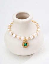Pearl bracelet with a green gemstone charm on a white vase