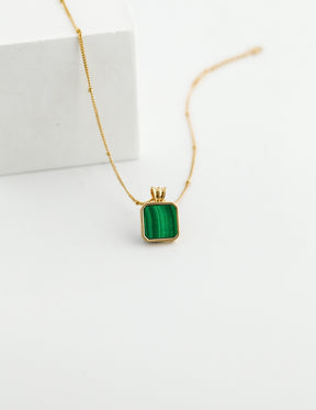 Gold necklace with a green malachite pendant on a white background