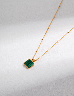 Gold necklace with a green malachite pendant on a light gray background