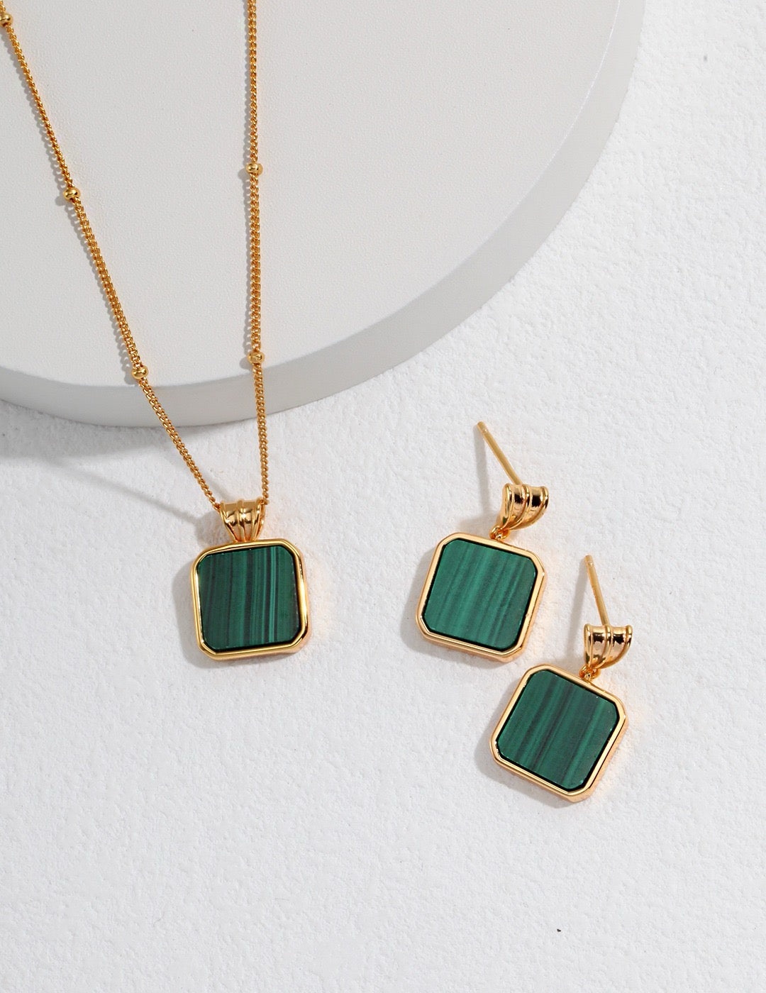 Gold necklace and earrings with green square malachite stones on a white background