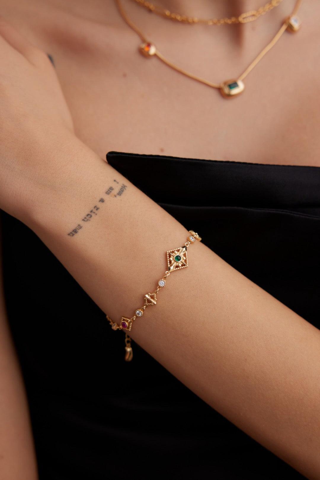 A person's wrist wearing a gold bracelet with small,egyptian-inspired turquoise stones.