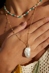 A 2.5cm Baroque pearl zircon necklace with a gold chain and a gold ornament, held between fingers.