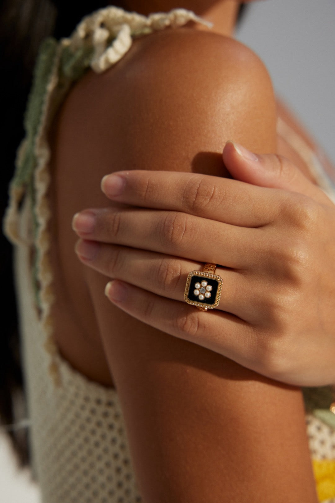 A close-up of a person's hand wearing a gold-colored open ring with a floral design on the finger.
